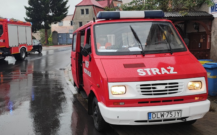Czerwony wóz strażacki zaparkowany na deszczowej ulicy.