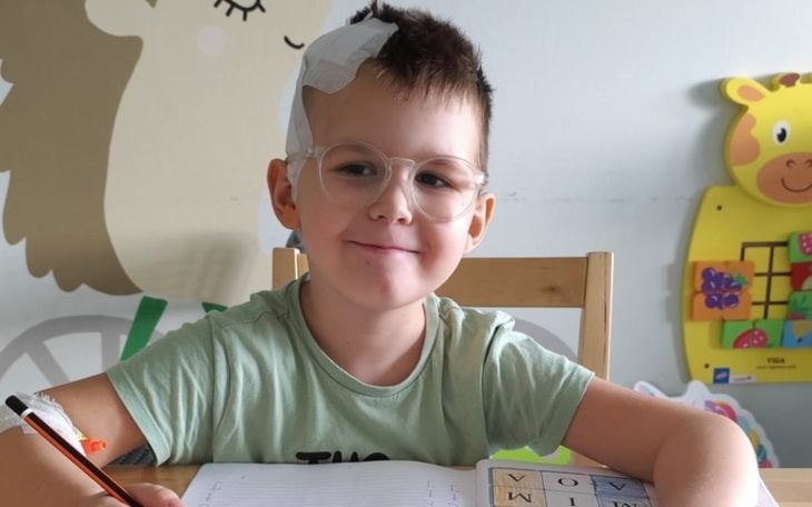 Chłopiec z opatrunkiem na głowie, uśmiechający się przy biurku.