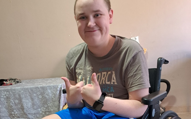 Młody chłopak w wózku inwalidzkim, uśmiechający się do kamery.