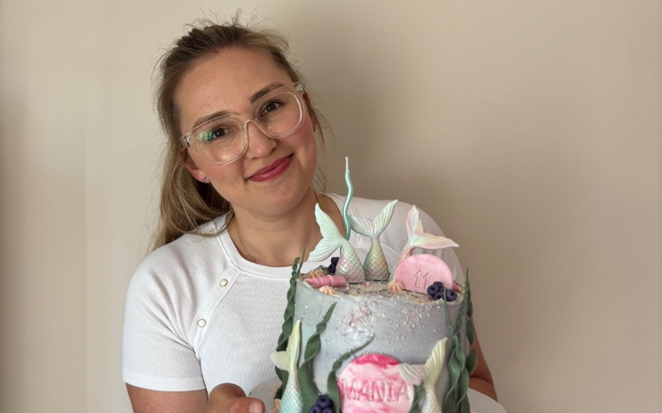 Kobieta trzymająca tort, uśmiechająca się do kamery.