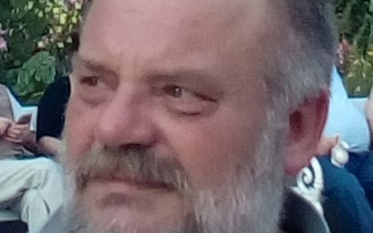 Mężczyzna z brodą, skupiony na rozmowie w plenerze.