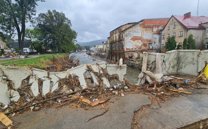 Zniszczony brzeg rzeki po powodzi, z ruinami budynków.
