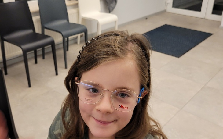 Dziewczynka w okularach, uśmiechająca się do kamery.
