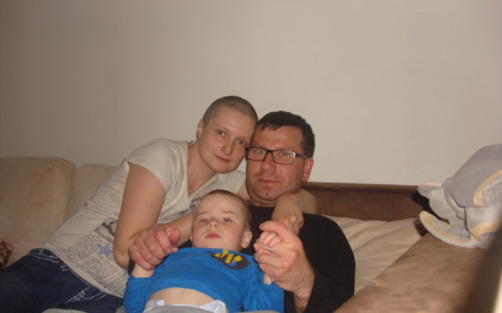 Rodzina na kanapie: mama, tata i mały chłopiec, wszyscy uśmiechnięci.