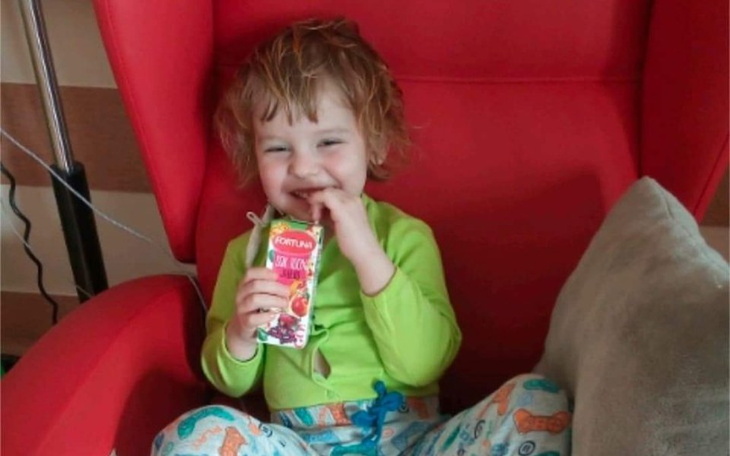 Mała dziewczynka siedząca w czerwonym fotelu z sokiem.