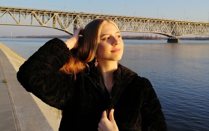 Kobieta na tle rzeki, w promieniach słońca, z mostem w tle.