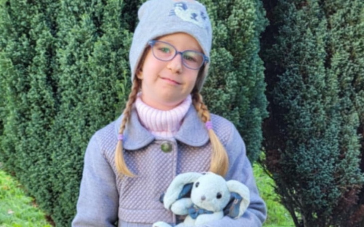 Dziewczynka w szarej czapce trzymająca pluszowego królika.