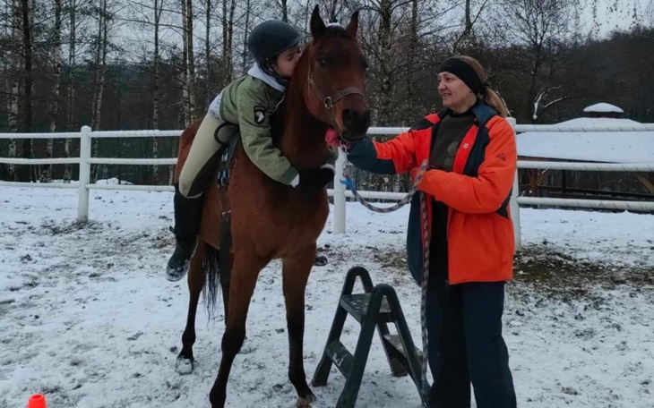 Dziecko na koniu, uśmiechnięta osoba w pomarańczowej kurtce.