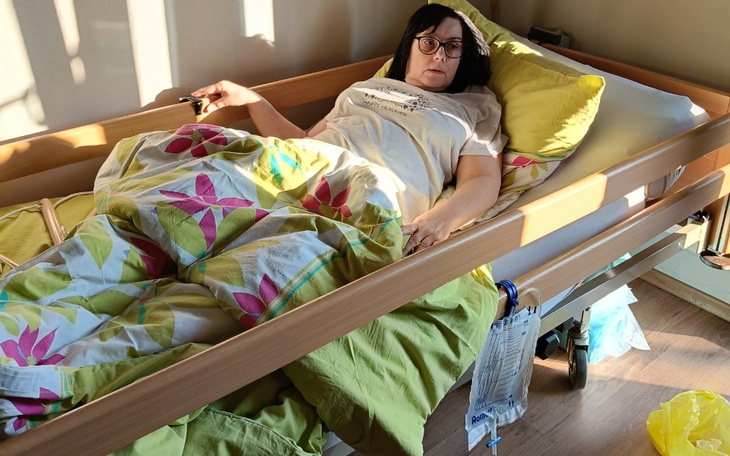 Kobieta leżąca w łóżku szpitalnym, otoczona kolorowymi pościelami.