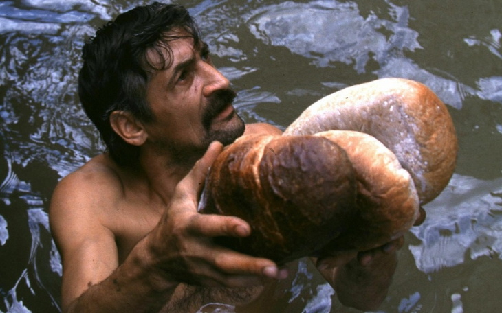 Mężczyzna trzyma bochenki chleba w wodzie, z wyrazem determinacji.