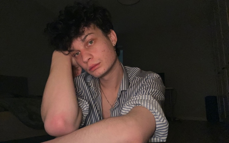 Młody mężczyzna z zamyśloną miną, siedzący w ciemnym pomieszczeniu.