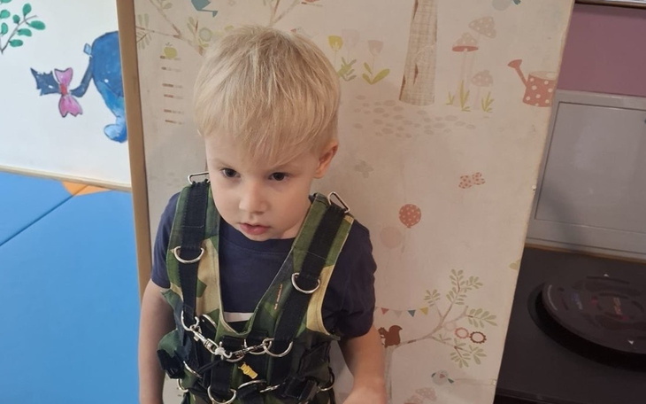 Chłopiec w uprzęży do wspinaczki, z poważnym wyrazem twarzy.