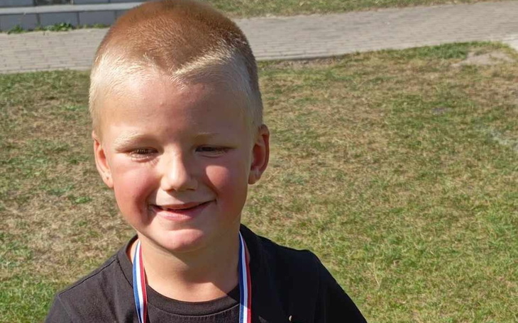 Chłopiec z medalem, uśmiechający się na tle trawy.