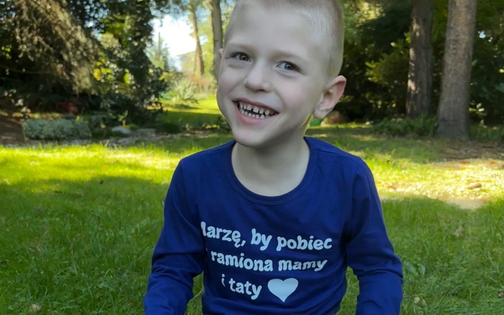 Chłopiec uśmiechający się na trawie, w niebieskiej koszulce.