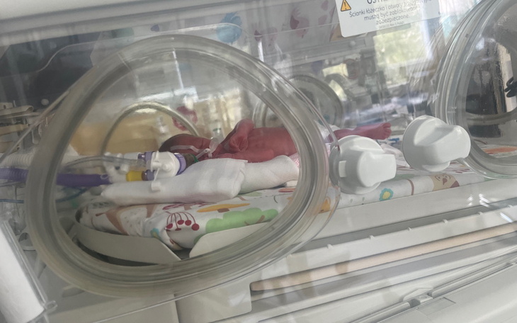 Noworodek w inkubatorze, otoczony sprzętem medycznym.