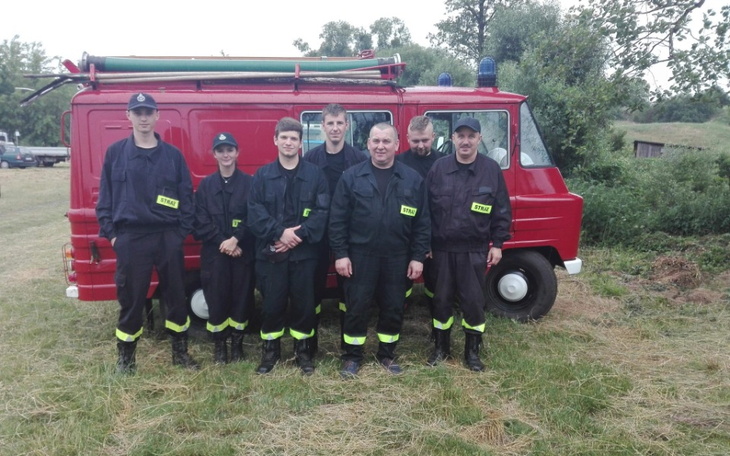 Grupa strażaków w mundurach obok wozu strażackiego.