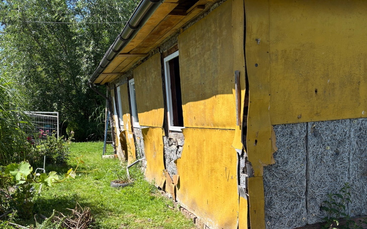 Zniszczony żółty dom z uszkodzoną elewacją, otoczony zielenią.