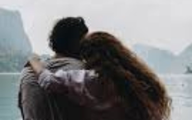 Para przytulająca się nad wodą, w tle góry.