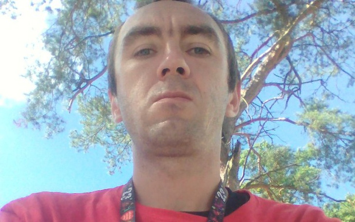 Mężczyzna na tle nieba i drzew, z poważnym wyrazem twarzy.