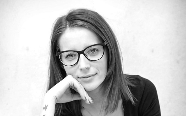 Portret młodej kobiety w okularach, z ręką na brodzie.