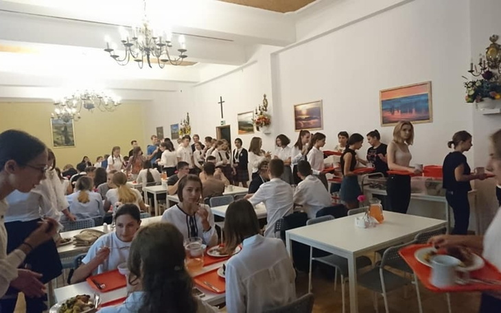 Zatłoczona stołówka z uczniami jedzącymi posiłki.