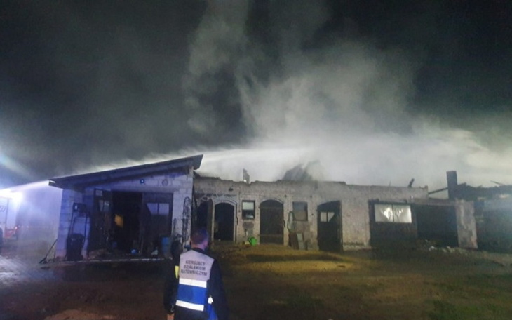 Zniszczony budynek w dymie po pożarze, z osobą w mundurze.