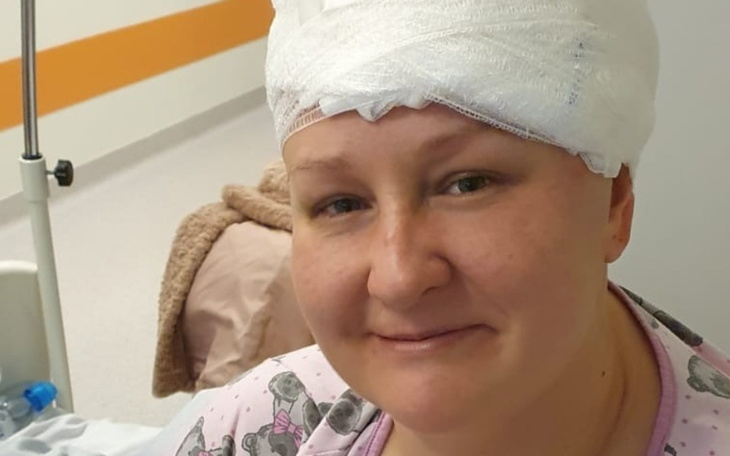 Kobieta w szpitalu z opatrunkiem na głowie, uśmiechająca się.