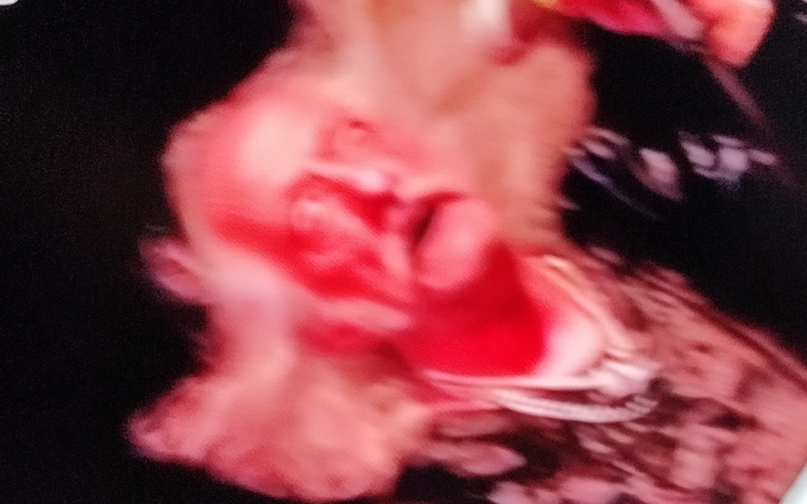 Osoba z wyrazistym makijażem, uśmiechająca się na tle ciemnego tła.