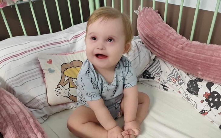 Uśmiechnięte dziecko siedzi w łóżeczku, otoczone poduszkami.