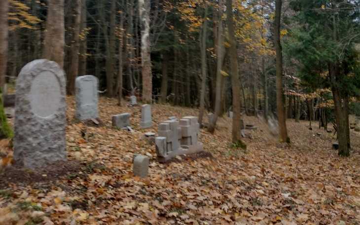 Zabytkowe nagrobki w lesie, otoczone jesiennymi liśćmi.