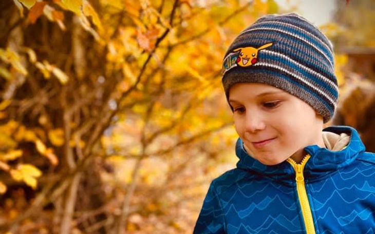 Chłopiec w czapce Pikachu, uśmiechający się wśród jesiennych liści.