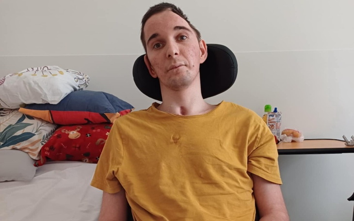 Mężczyzna w żółtej koszulce siedzi na wózku, otoczony poduszkami.