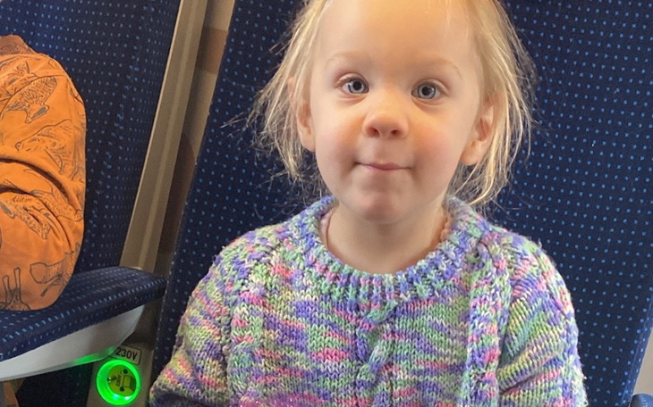 Mała dziewczynka w kolorowym swetrze, uśmiechająca się.