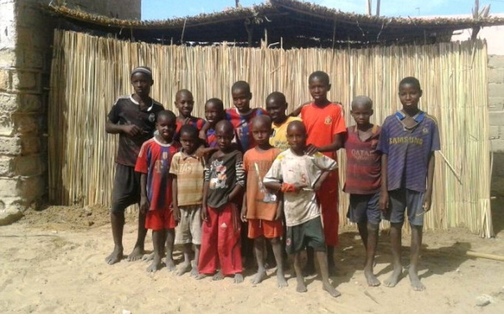 Grupa dzieci w kolorowych strojach, pozujących przed chatką.