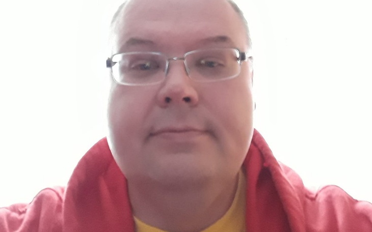 Mężczyzna w czerwonej bluzie, z uśmiechem na twarzy.