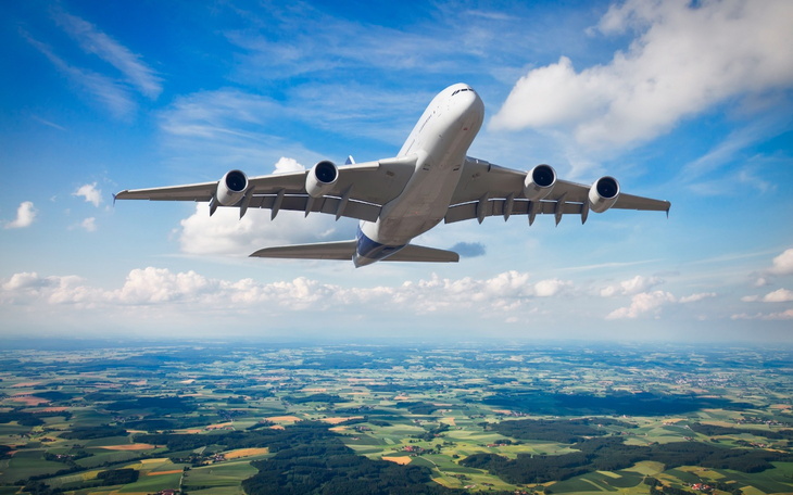 Samolot w locie, nad zielonymi polami i niebieskim niebem.