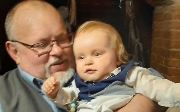 Dziecko w objęciach dziadka, oboje uśmiechnięci w przytulnej atmosferze.
