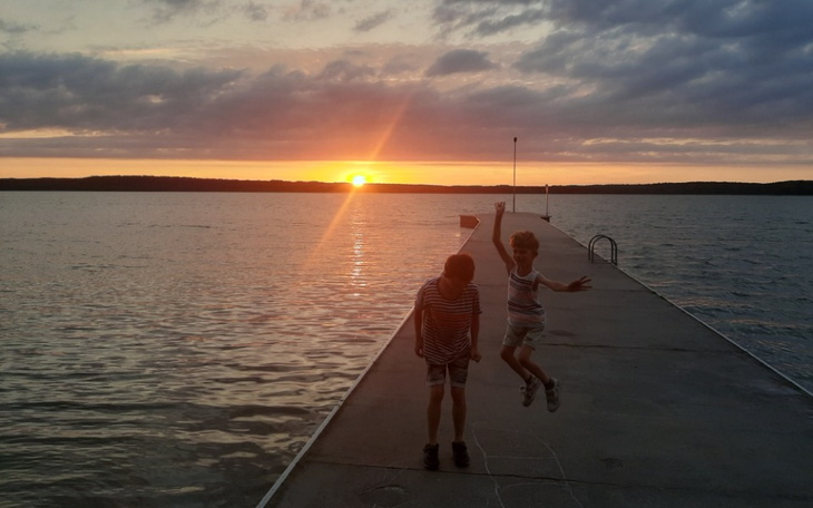Dzieci skaczące na pomoście podczas zachodu słońca.
