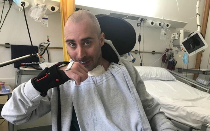 Mężczyzna w szpitalu, uśmiechający się i trzymający rękę na twarzy.