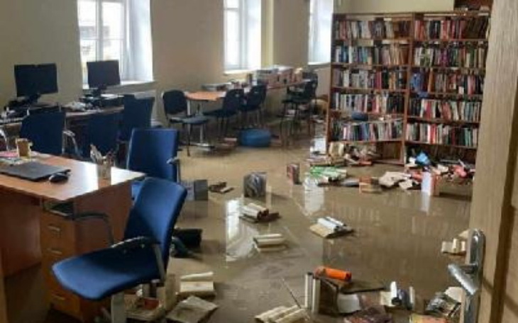 Zalane biuro z przewróconymi książkami i meblami.