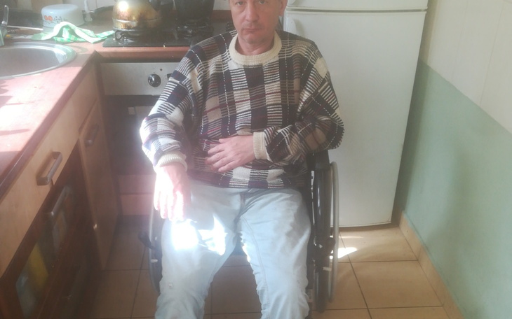 Mężczyzna na wózku inwalidzkim w kuchni, z poważnym wyrazem twarzy.