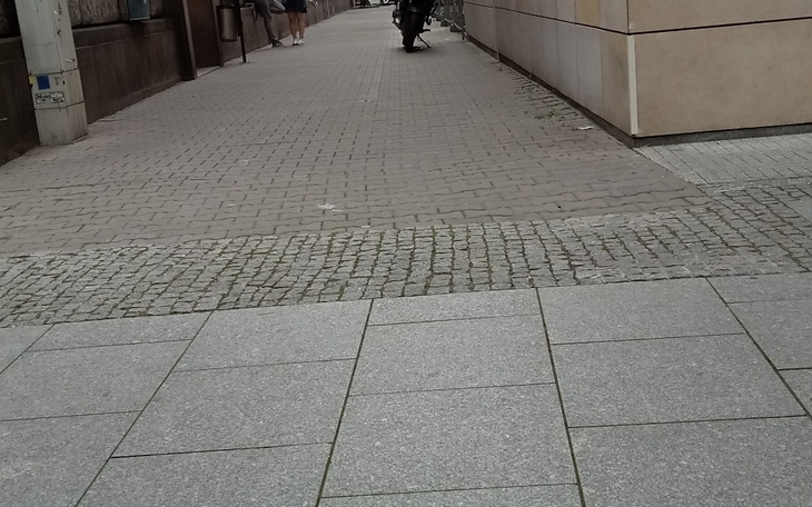 Osoba spaceruje w mieście, potykacz i chodnik w tle.