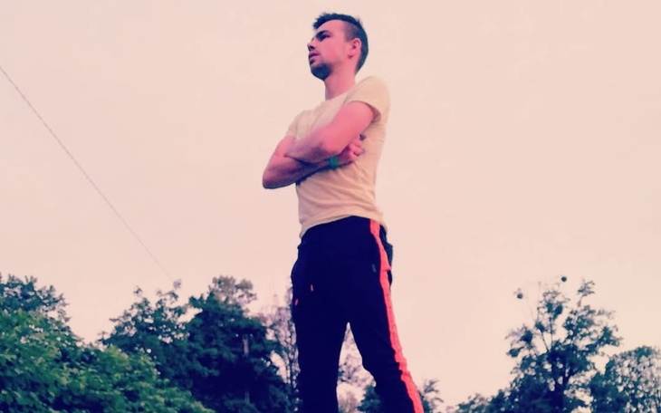 Mężczyzna stojący na tle zieleni, z rękami skrzyżowanymi.