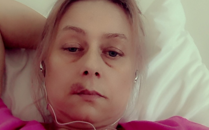 Portret kobiety w różowej koszulce, leżącej na łóżku, z słuchawkami na uszach.