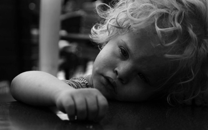 Mały chłopiec z kręconymi włosami, smutny na stole.