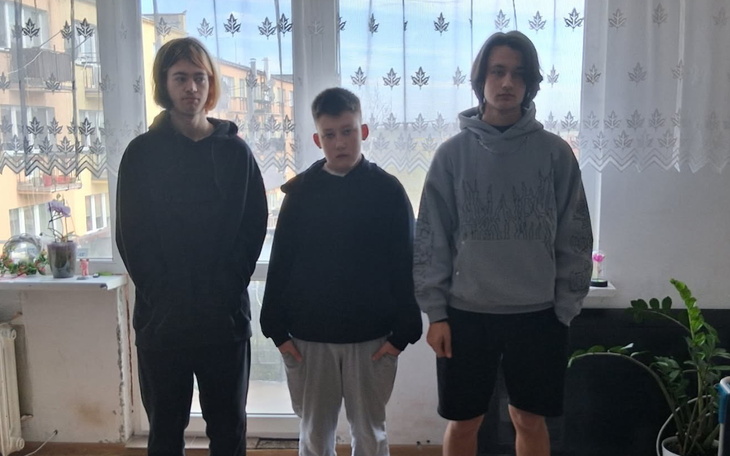 Trzech nastolatków stojących w pokoju, ubranych w luźne ubrania.