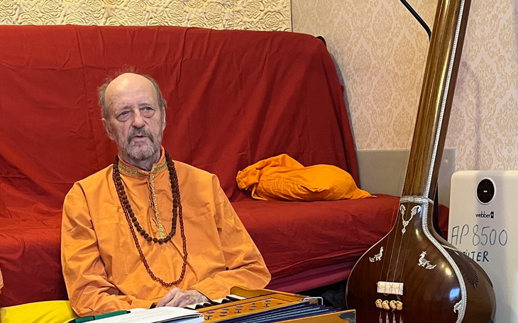 Mężczyzna w pomarańczowym stroju medytacyjnym z instrumentem muzycznym.