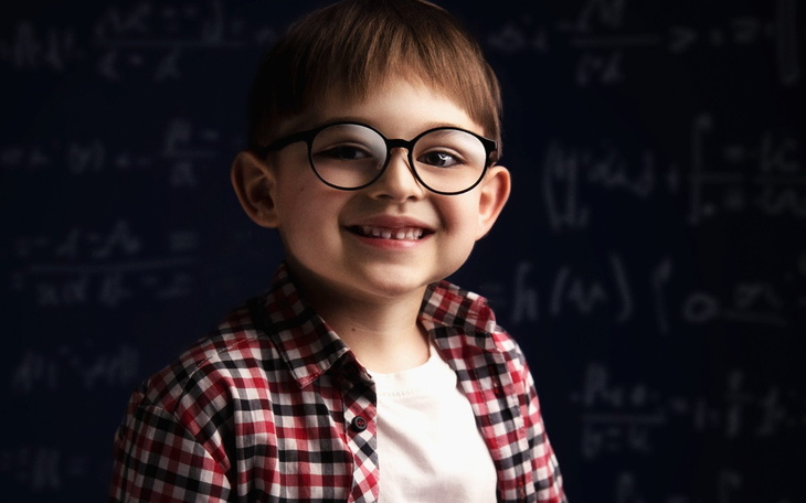 Uśmiechnięty chłopiec w okularach, pozujący na tle matematycznych wzorów.