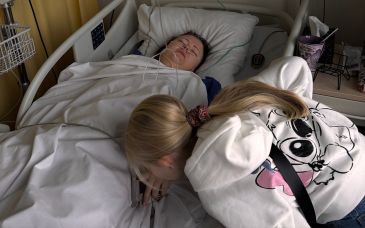 Dwie dziewczynki przy łóżku szpitalnym, jedna z telefonem.