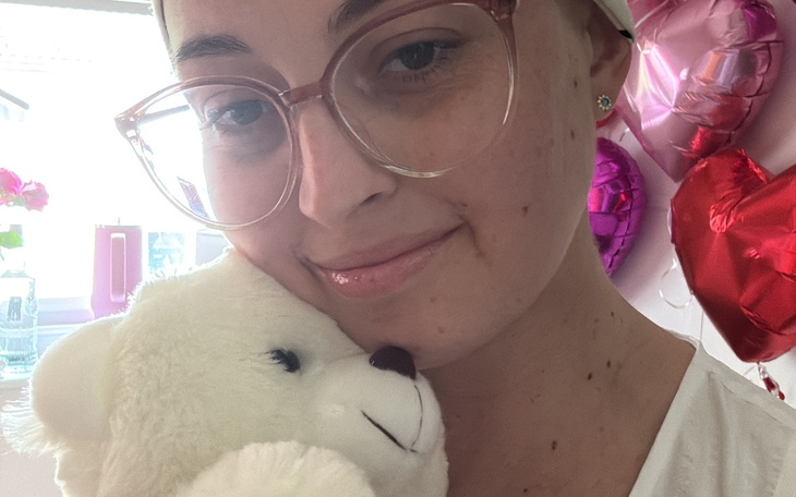 Kobieta przytula pluszowego misia, otoczona balonami.